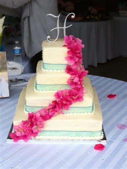 Four tier square white cake with light blue strips and pink flowers.
