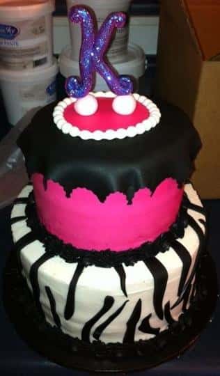 Two tier cake that is black, bright pink and white with the letter K on top.