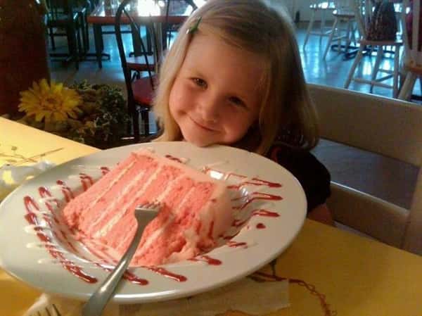 Young girl smiling at the camera with a cake in front of here.