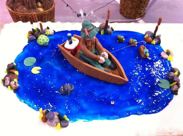 White cake with blue icing representing a pond with a man in a boat on top.
