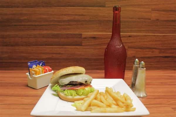 Cheeseburger topped with Swiss cheese with lettuce, tomato and onion. French fries, salt, pepper, sauces and unopened bottle of rose on the side.