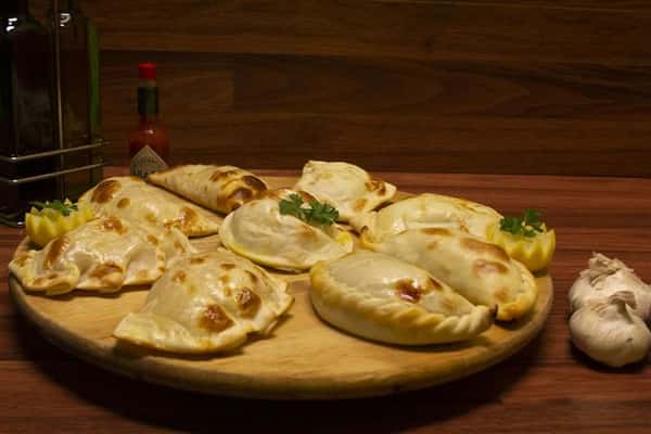Assorted empanadas on a wood tray. Garlic, red onion, Tabasco Hot Sauce and olive oil on the side.