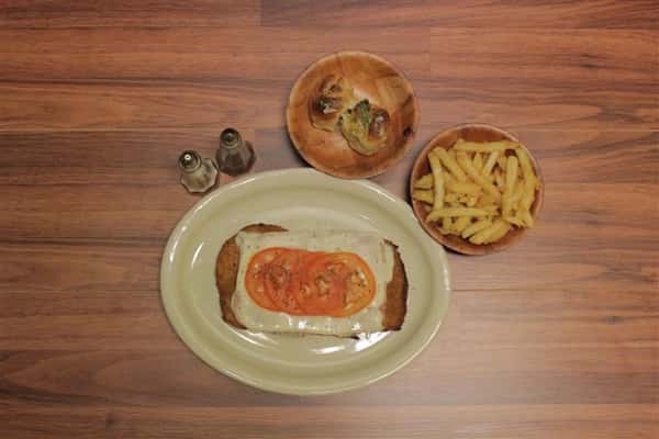 Top view of Chicken Parmigiana topped with melted mozzarella cheese and a touch of tomato sauce. Garlic knots and small Caesar salad on the side.