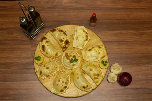 Top View of assorted empanadas on a wood tray. Garlic, red onion, Tabasco Hot Sauce and olive oil on the side.