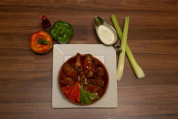 Top view of Chicken wings in a bowl with a bottle of Tabasco sauce, bell peppers, celery and side of bleu cheese.