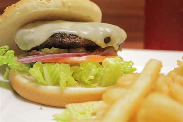 Cheeseburger topped with Swiss cheese with lettuce, tomato and onion. French fries on the side.