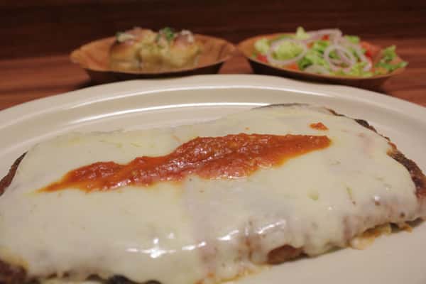 Chicken Parmigiana topped with melted mozzarella cheese and a touch of tomato sauce. Garlic knots and small salad on the side.
