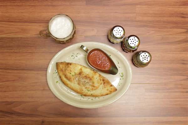 Top view of Calzone on a plate with a side of marinara sauce. Beer stein and spices on the side.