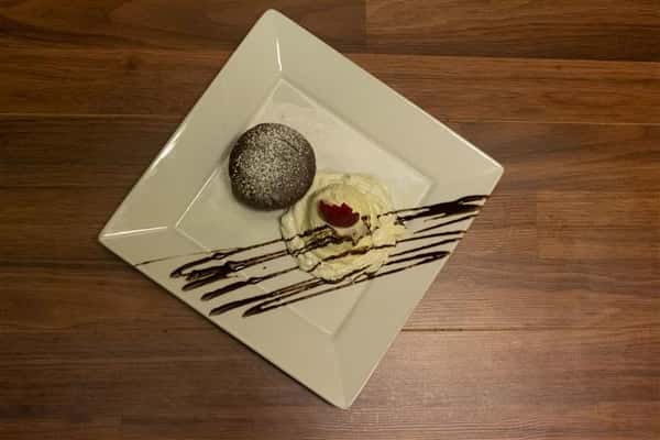 Top view of Chocolate Souffle on a square plate with a scoop of vanilla ice cream on the side. Ice cream topped with a strawberry and chocolate syrup drizzle.