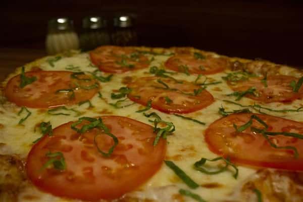 Close up view of Caprese Pizza. Pizza topped with tomato sauce, mozzarella, sliced tomato, Italian sausage, black olives, oregano & virgin olive oil.