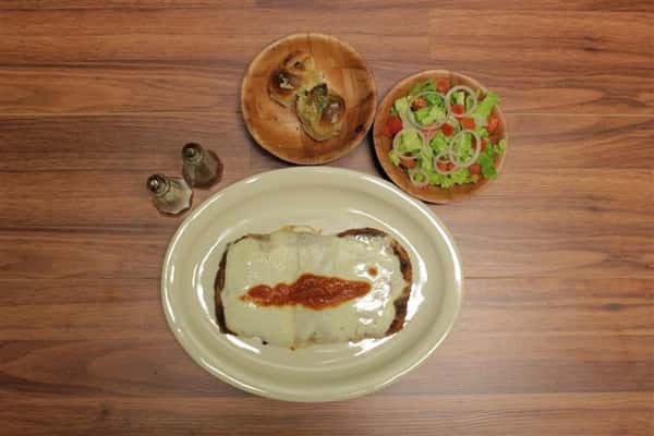 Top view of Chicken Parmigiana topped with melted mozzarella cheese and a touch of tomato sauce. Garlic knots and small salad on the side.