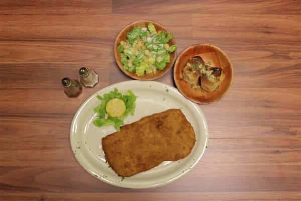 Top view of Chicken Milanase plate. Small Caesar salad and garlic knots on the side.