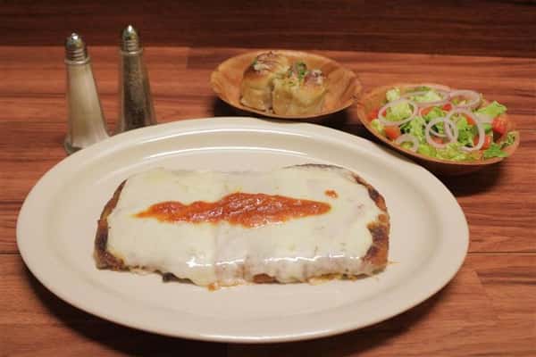 Chicken Parmigiana topped with melted mozzarella cheese and a touch of tomato sauce. Garlic knots and small salad on the side.