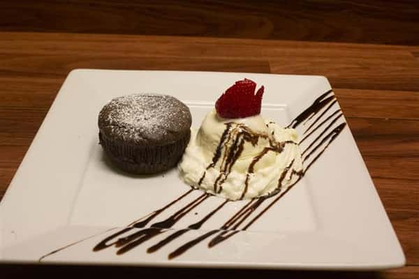 Chocolate Souffle on a square plate with a scoop of vanilla ice cream on the side. Ice cream topped with a strawberry and chocolate syrup drizzle.
