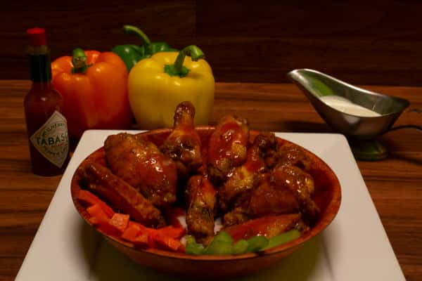 Chicken wings in a bowl with a bottle of Tabasco sauce, bell peppers, celery and side of bleu cheese.