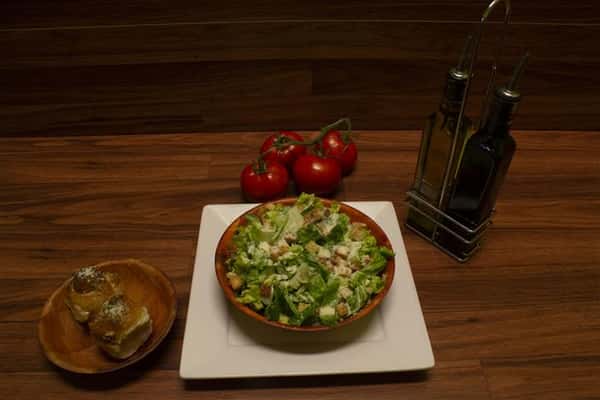 Top view of Caesar Salad with olive oil, garlic knots and tomatoes on the vine on the side.