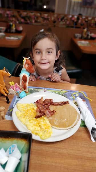 Girl posing for picture with plate of pancakes eggs and bacon