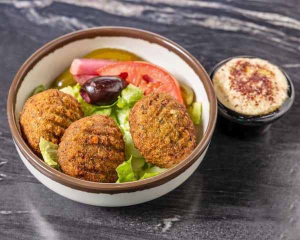 Crispy falafel served over fresh lettuce with tomatoes, pickles, and Kalamata olives, accompanied by a side of creamy hummus for a classic Mediterranean vegetarian meal.