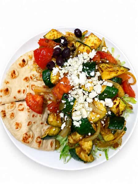 Mediterranean grilled vegetable platter with zucchini, tomatoes, onions, feta cheese, Kalamata olives, and warm pita bread served over fresh lettuce.