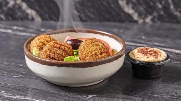 Mediterranean falafel bowl with crispy falafel, fresh vegetables, Kalamata olives, and a side of creamy hummus.
