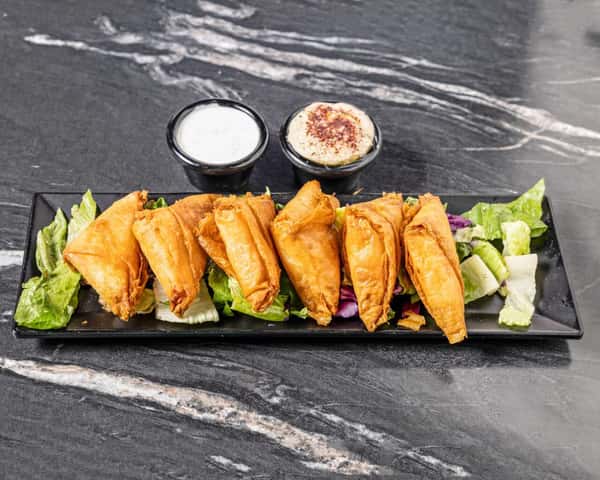 Crispy Mediterranean spanakopita triangles served on a bed of fresh lettuce with creamy garlic sauce and hummus, offering a savory Greek-inspired appetizer.