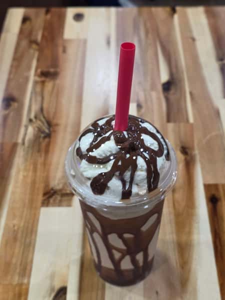 Chocolate milkshake topped with whipped cream and chocolate drizzle in a clear cup – indulgent ice cream shop drink with rich cocoa syrup and thick red straw.