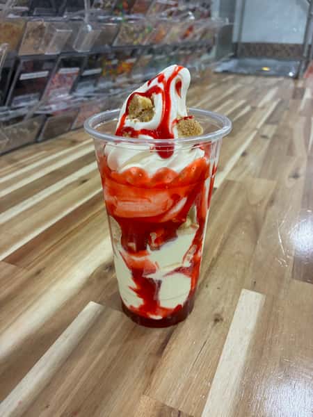 Strawberry cheesecake frozen yogurt parfait layered with fresh strawberry sauce and graham cracker crumble in a clear cup – sweet, tangy dessert perfect for a froyo bar topping station.