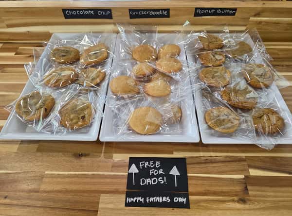 Assorted bakery cookies individually wrapped and labeled chocolate chip, snickerdoodle, and peanut butter – Father's Day cookie display with "Free for Dads" sign.
