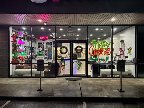Frozen yogurt shop storefront at night decorated with festive Christmas window art and neon open sign – holiday-themed dessert café exterior ideal for seasonal promotions and local business listings.