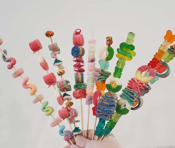 Colorful candy skewers featuring gummy worms, sour belts, marshmallows, and assorted chewy candies on wooden sticks – fun party treats and sweet shop favorites ideal for kids' celebrations and candy buffets.