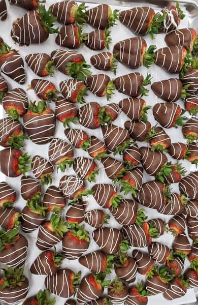 Chocolate-covered strawberries with white chocolate drizzle arranged on a bakery tray – gourmet dark chocolate dipped strawberries with fresh green tops, perfect for Valentine's Day gifts, wedding dessert tables, or chocolate shop catering displays.