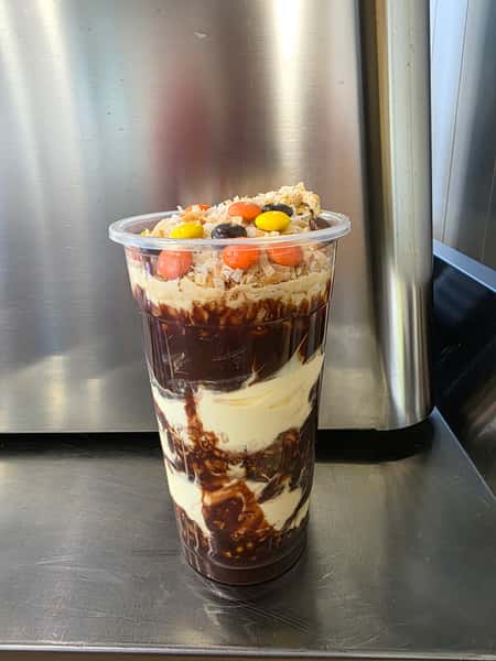 Layered peanut butter and chocolate frozen yogurt parfait in a clear cup, swirled with rich fudge sauce and topped with shredded coconut and colorful candy pieces – indulgent dessert cup perfect for a frozen yogurt shop or ice cream café menu.
