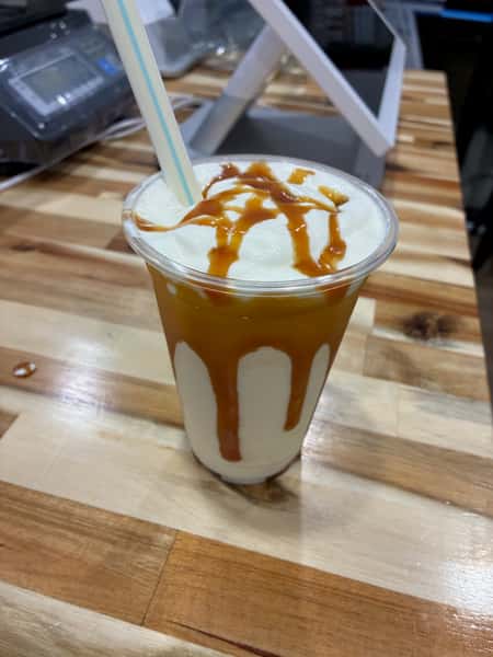 Caramel milkshake topped with whipped cream and rich caramel drizzle in a clear cup – creamy blended dessert drink perfect for an ice cream shop or froyo café.