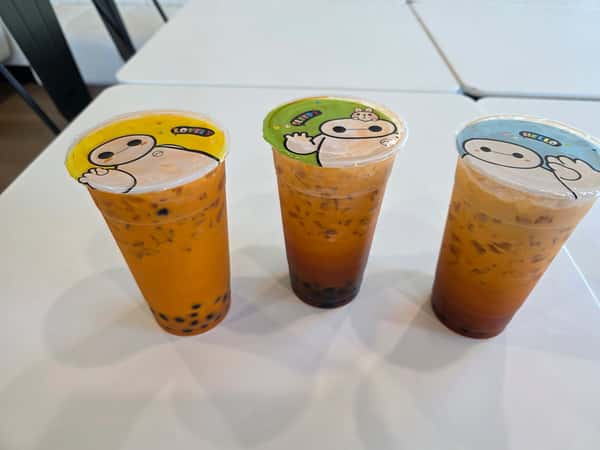 Three iced milk tea bubble teas with tapioca pearls in clear cups with sealed cartoon lids – refreshing boba drinks perfect for a modern dessert café or tea shop.