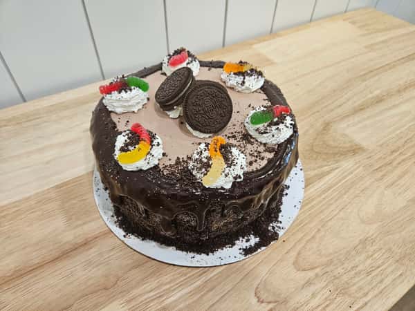 Chocolate Oreo drip cake topped with cookies and cream frosting, whole Oreo cookies, chocolate ganache, and colorful gummy worms – decadent chocolate layer cake with cookie crumble coating, perfect for a bakery dessert display or birthday celebration.