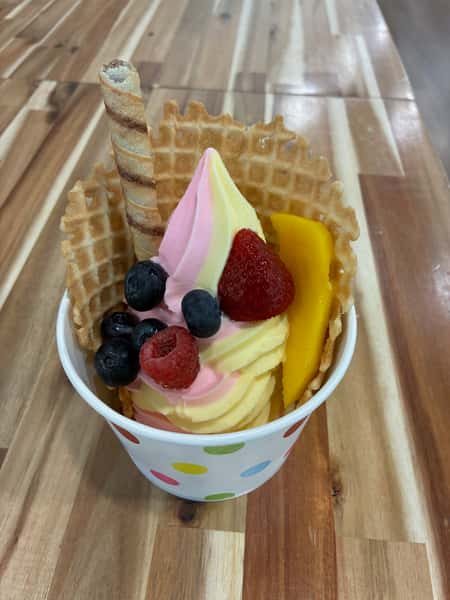 Strawberry and vanilla swirl soft serve frozen yogurt topped with fresh blueberries, raspberry, sliced strawberry, and mango, served in a waffle bowl with a rolled wafer cookie – colorful summer dessert perfect for a frozen yogurt shop or ice cream café.