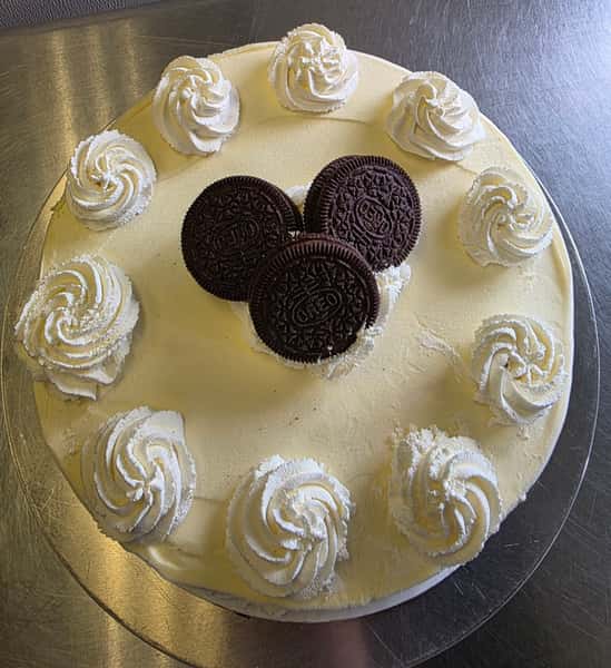 Oreo cookies and cream ice cream cake topped with whipped frosting rosettes and whole chocolate sandwich cookies – classic celebration dessert on a bakery cake stand.