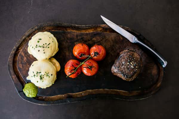 Steak and tomato on wooden plate