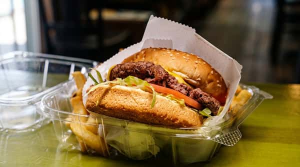 Juicy cheeseburger with lettuce, tomato, and crispy fries served in a takeout container