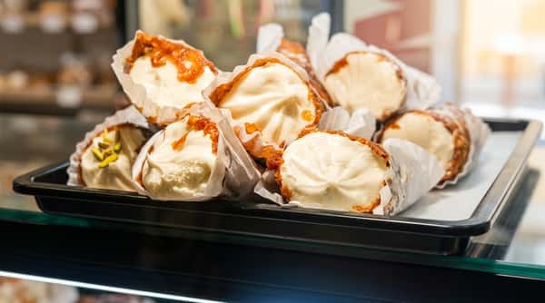 Fresh cannoli pastries filled with sweet ricotta cream, displayed in a bakery case and garnished with pistachios and crispy pastry shells.