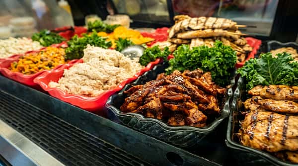Fresh salad bar featuring grilled chicken, barbecue chicken, shredded chicken, and colorful vegetables in a restaurant buffet display