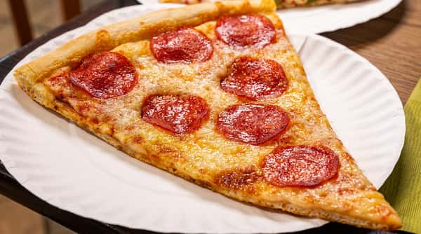 Oversized slice of pepperoni pizza with melted mozzarella cheese and a thin crispy crust served on a paper plate