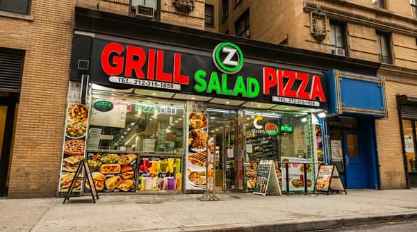 Storefront of "Grill Z Salad Pizza" with red and green neon signage above large display windows showing food items.
