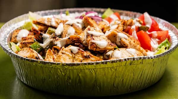 Grilled chicken rice bowl with seasoned chicken, fresh lettuce, tomatoes, cucumbers, red onions, and creamy garlic sauce, served in a Mediterranean-style takeout bowl.