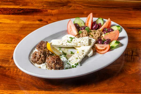 Mediterranean platter with seasoned meatballs, feta, tzatziki, olives, tomatoes, cucumbers, and savory dip.