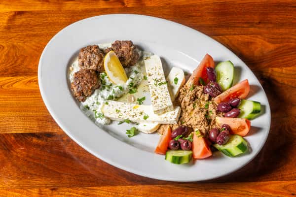 Mediterranean platter with grilled meatballs, feta cheese, tzatziki, olives, tomatoes, cucumbers, and savory dip.