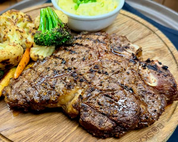 Grilled bone-in ribeye steak served with roasted vegetables and dipping sauce at an upscale American restaurant