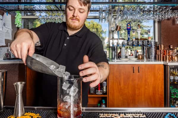 Bartender adding ice to a mixing glass while preparing a handcrafted cocktail at the restaurant bar.