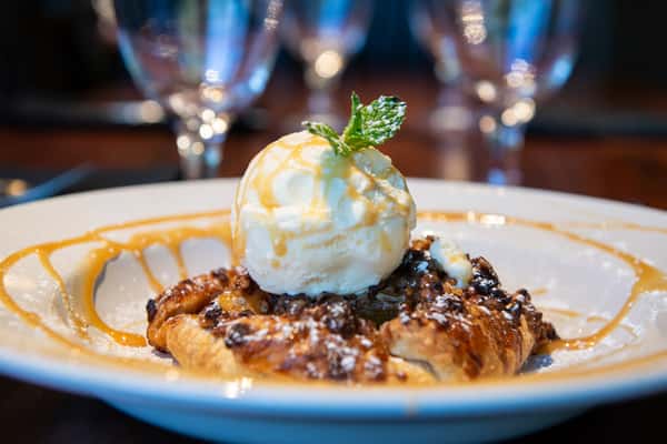 Warm dessert topped with vanilla ice cream and caramel drizzle served in an elegant restaurant setting