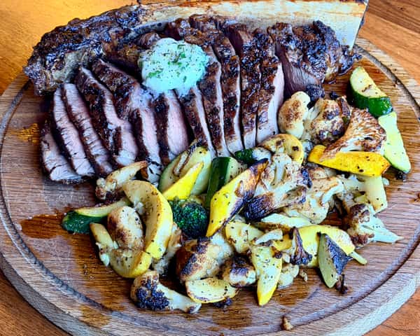 Charbroiled steak with grilled vegetables and herb butter served on a wooden platter
